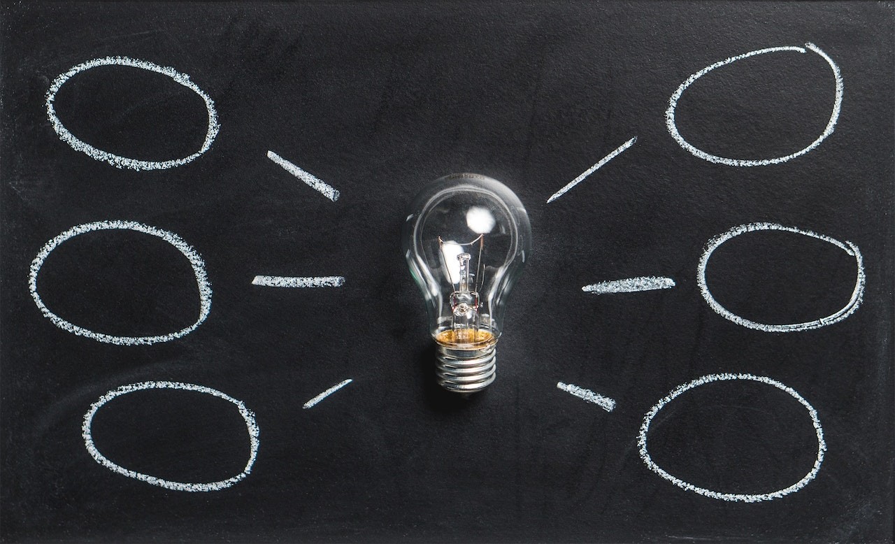 light bulb against balcboard with thought bubbles sketched on the board