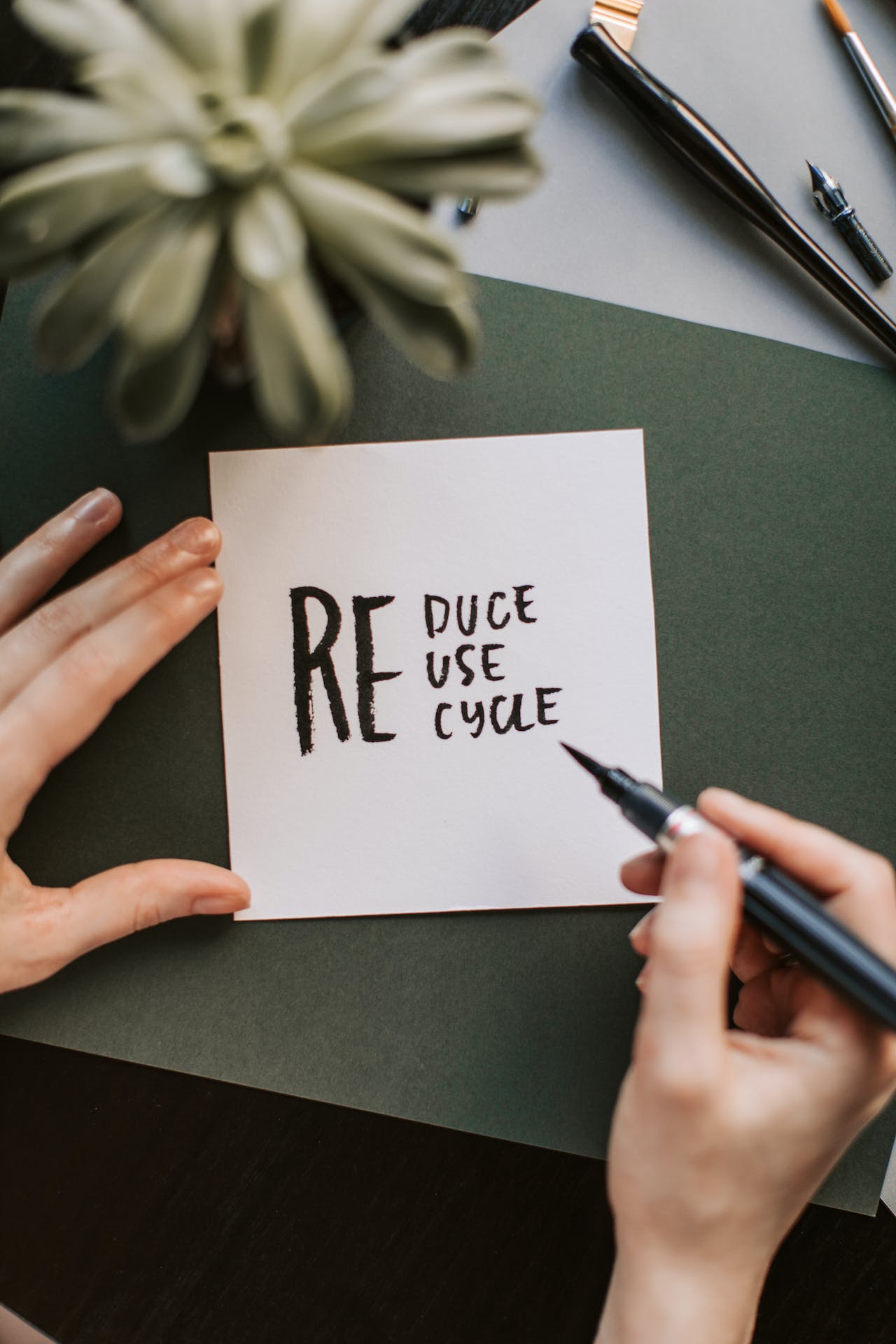 hand with pen writing "Reduce, Reuse, Recycle" on post it note